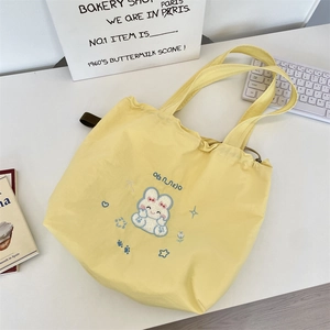 Detail of light yellow drawstring tote bag with cute white rabbit embroidery on desk