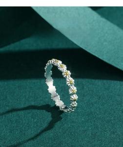 Detailed view of silver daisy flower ring with yellow accents on a dark green background