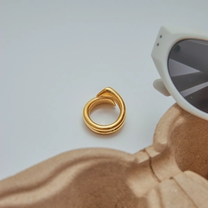 Nahaufnahme des minimalistisch vergoldeten Edelstahlrings in gedrehtem Design auf grau