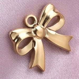 Macro shot of 304 stainless steel golden bow pendant on glossy purple silk fabric