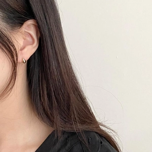 Close-up of a minimalist golden teardrop earring worn on ear with metallic finish