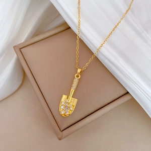Elegant gold shovel necklace with rhinestones on beige display box and white silk fabric
