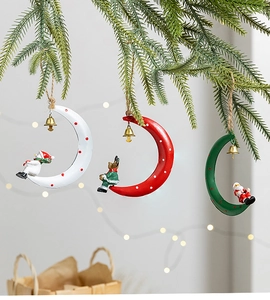 Three moon-shaped Christmas ornaments with bells and figurines on pine branches
