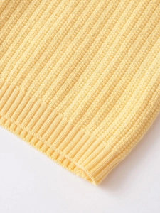 Macro shot of pale yellow knit cardigan showing ribbed cuffs and honeycomb texture