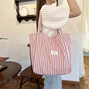 Detail of red and white striped canvas tote bag worn on shoulder in a cozy cafe setting