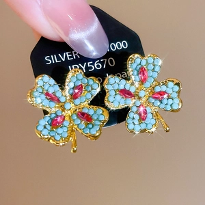 Macro view of gold four-leaf clover stud earrings with blue beads and red marquise stones