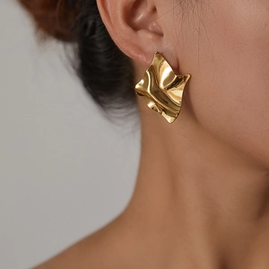 Close-up of golden irregular wavy textured earrings on model with metallic finish