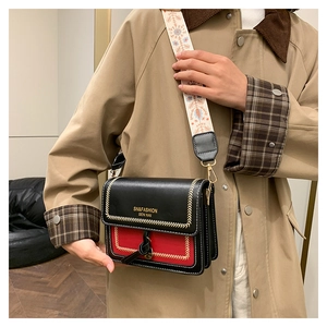 Close-up of red crossbody bag with black flap and geometric embroidered strap