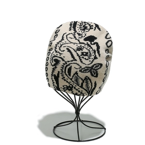 Détail du bonnet en tricot beige avec motif Paisley noir sur un support de présentation