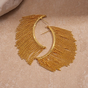 Close-up of golden C-shaped tassel earrings with metallic beaded chains on stone