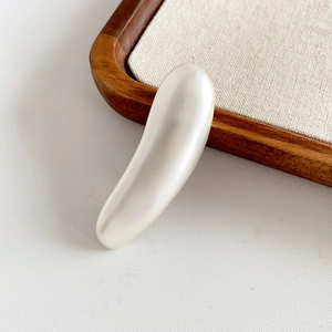 Close-up of a minimalist pearl white resin accessory on a textured wooden tray background