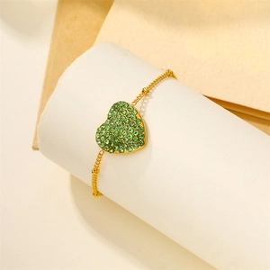Detailed view of an 18k gold heart bracelet with green crystals wrapped on a white prop