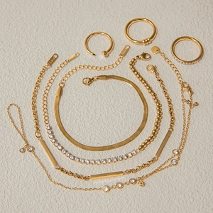 Detailed close-up of golden stainless steel jewelry set with bracelets and rings on a textured background