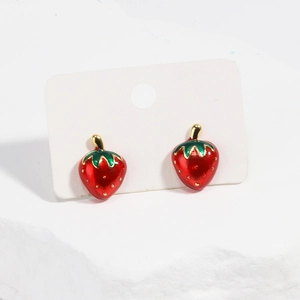 Gros plan de boucles d'oreilles fraises en émail rouge avec feuilles dorées sur socle