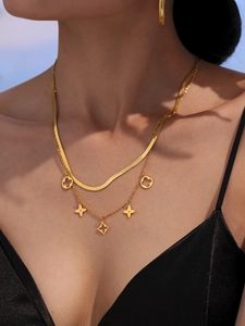 Détail d'un collier doré multicouche avec trèfles à quatre feuilles et boucles d'oreilles créoles