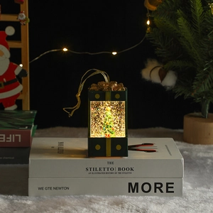 Close-up of a lit green Christmas lantern with a miniature tree and swirling glitter inside