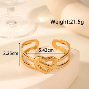 Elegant gold double heart open cuff bracelet displayed on a minimalist geometric pedestal