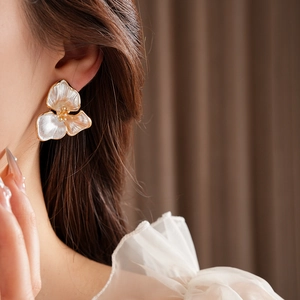 Detail of elegant white pearl shell flower earrings on model with golden accents
