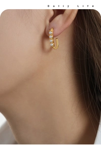 Detailed view of U-shaped gold plated steel earrings with five inlaid white pearls