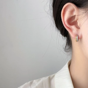 Close-up of gold and silver two-tone stainless steel hoop earrings on a female model