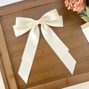 Close-up of a cream white satin bow hair clip on a wooden tray with dried flowers
