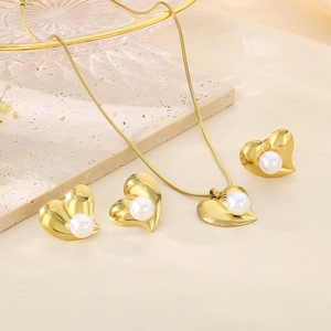 Close-up of golden heart-shaped jewelry set with white pearls on a stone tray