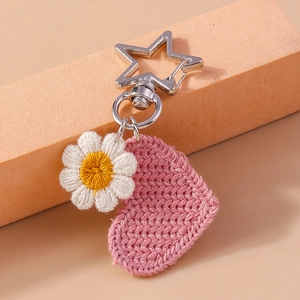 Macro detail of hand-knitted pink heart and white daisy flower keychain with silver star clip