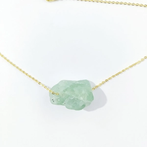 Detailed view of irregular green crystal pendant on a delicate gold chain necklace