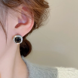 Close-up of square black gemstone stud earring with clear crystal halo in silver finish