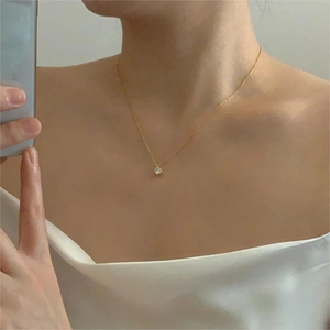 Detail of a minimalist gold zircon pendant necklace worn by a model in warm light