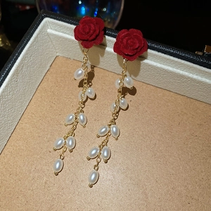 Detail view of red flocked rose earrings with dangling white pearl tassels in a box