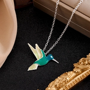 Macro view of hummingbird necklace with green enamel pendant on a premium black background