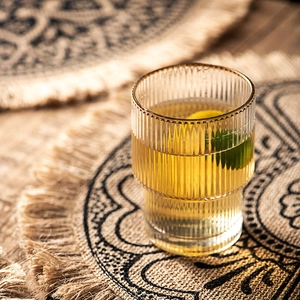 Japanese woven jute placemat with tassels featuring a ribbed gold-rimmed glass cup