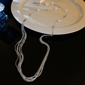 Detail of silver multi-layer layered necklace with white pearls on white ceramic plate