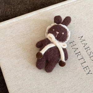 Detailed macro of brown felt rabbit brooch with cream lace collar and knit bow detail