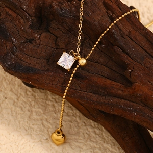Detail view of 18K gold plated square zircon necklace with heart charm on a wooden block