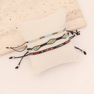 Close-up of three handmade bohemian woven seed bead bracelets on a white pillow display