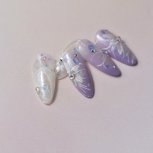 Detail of gradient purple and milky white press-on nails with white flower and rhinestones