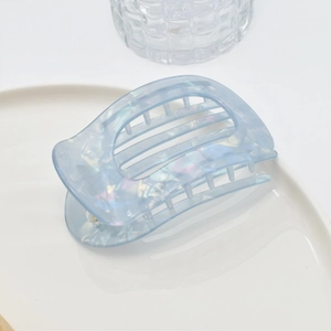 Close-up of light blue acetate hair claw with marble texture on white ceramic plate
