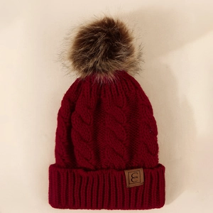 Detailed knit cable pattern on burgundy winter beanie with faux fur pom and leather tag
