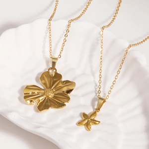 Goldene Blumen- und Seesternanhänger in einer weißen muschelförmigen Keramikschale