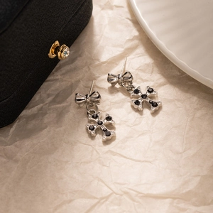 Détail de boucles d'oreilles nœud et croix argentées avec strass noirs sur boîte à bijoux