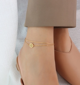 Close-up of double-layer gold anklet with snake chain and stylized Fu pendant on ankle