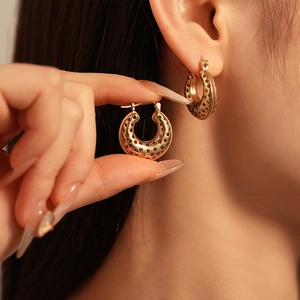 Détail de boucles d'oreilles dorées en C avec motifs étoiles portées par le mannequin