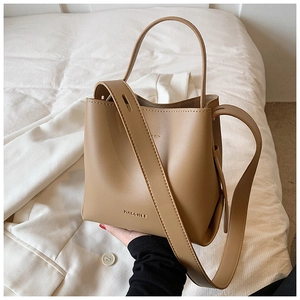 Close-up of camel brown leather bucket bag with embossed logo held by hand