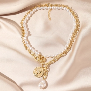 Detail of layered gold coin necklace and baroque pearl pendant on champagne silk fabric