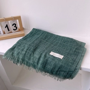 Detail of green linen scarf with fringe edges and Autumn On Line label on white surface