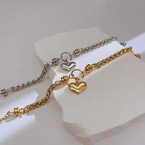 Macro detail of gold and silver heart pendant bracelets on textured white stone background