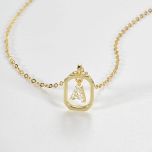 Macro detail of gold necklace featuring a rectangular frame and crystal letter A pendant