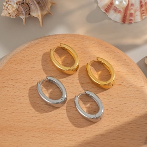 Close-up of gold and silver U-shaped hoop earrings on a wooden stand with shells